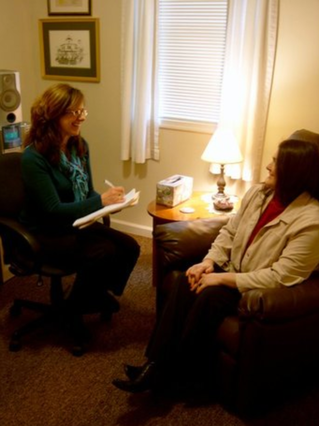 Rev. Flynn with a female client in her office taking notes during a pre-session interview.